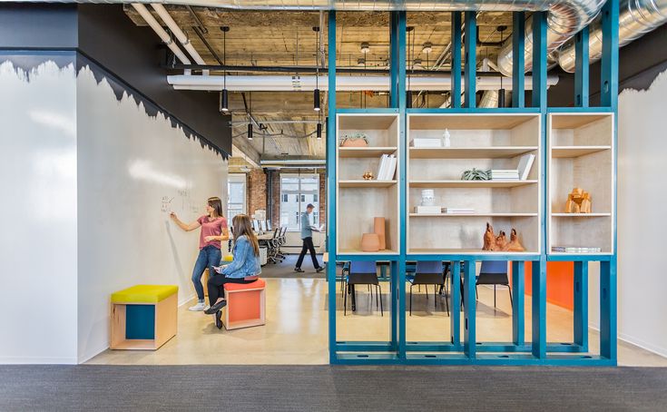 two people are sitting on stools in an open space with shelves and shelving