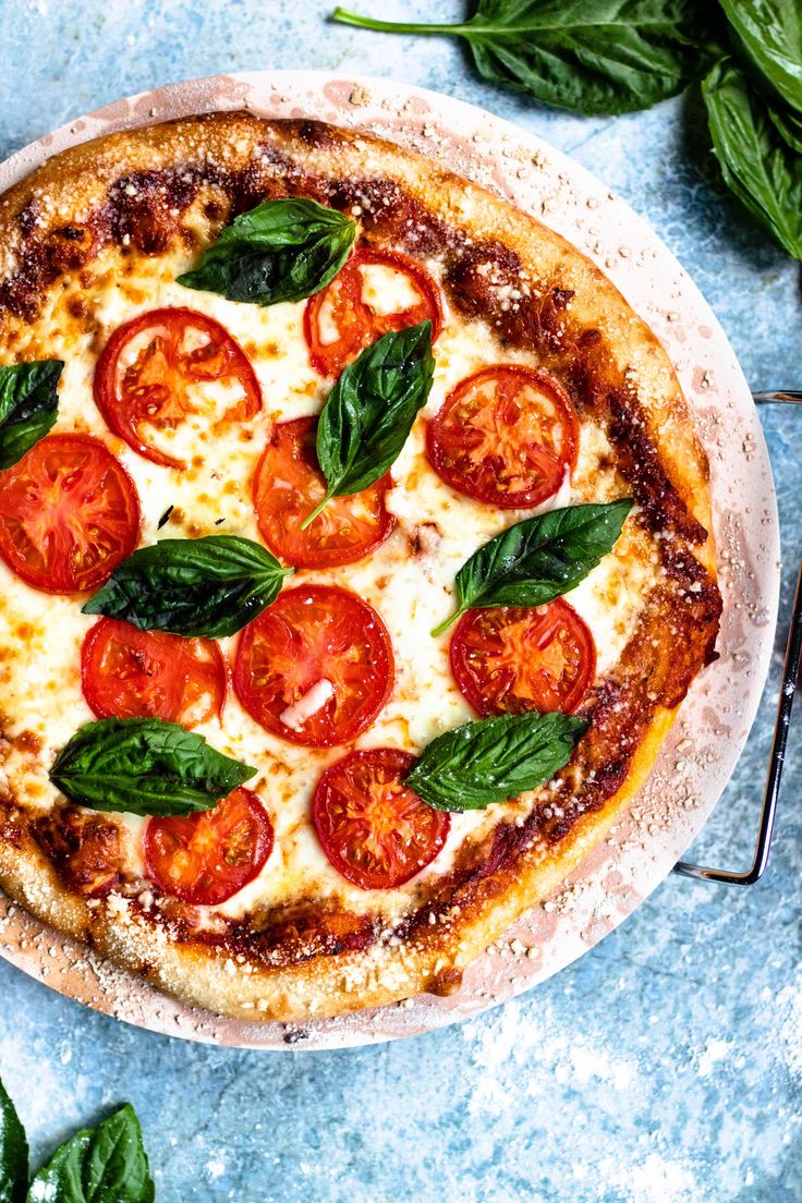 a pizza topped with tomatoes and basil on top of a white plate next to green leaves