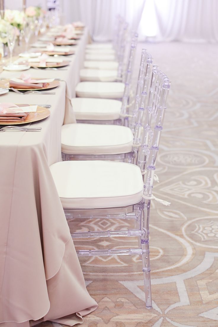 a long table set up with white chairs and pink napkins on top of it