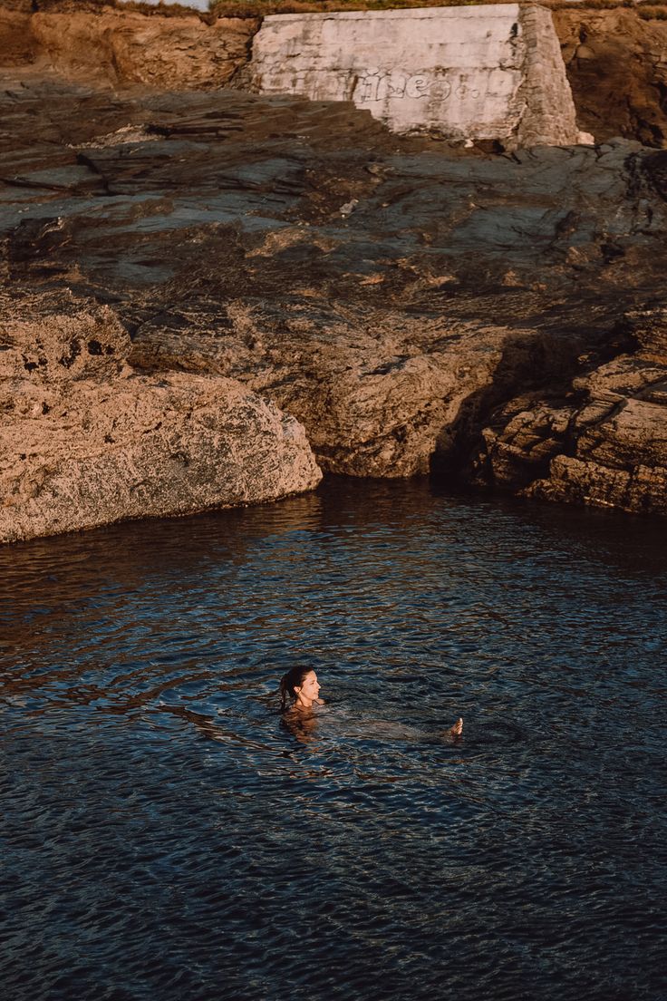 a person swimming in the water near some rocks