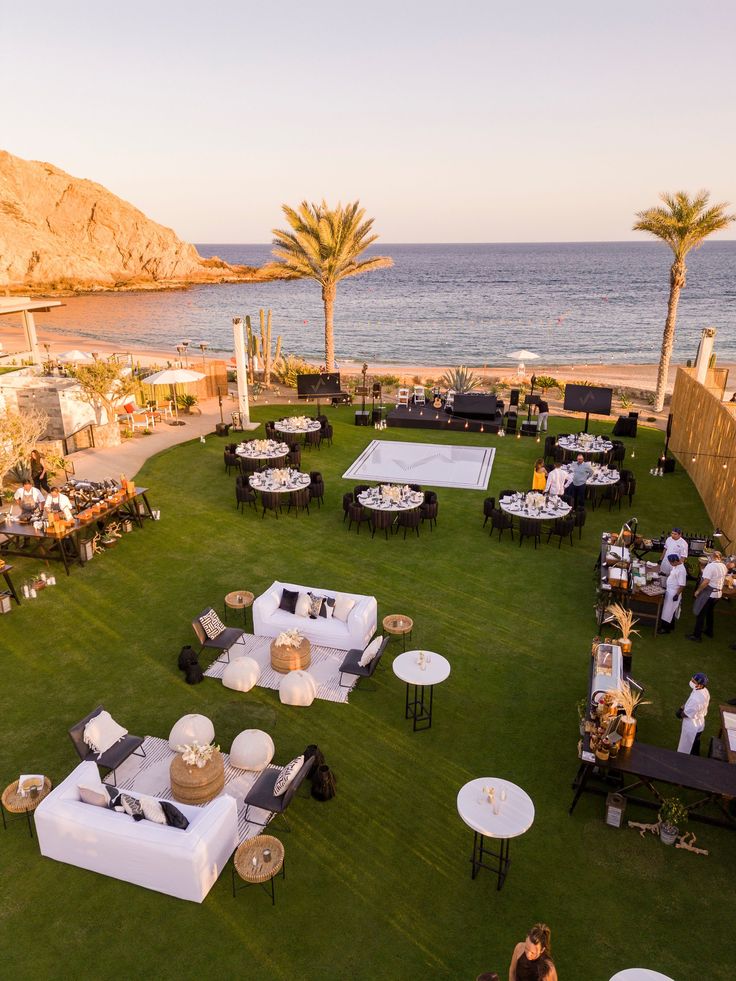 an aerial view of a lawn with tables and chairs set up on the grass near the ocean