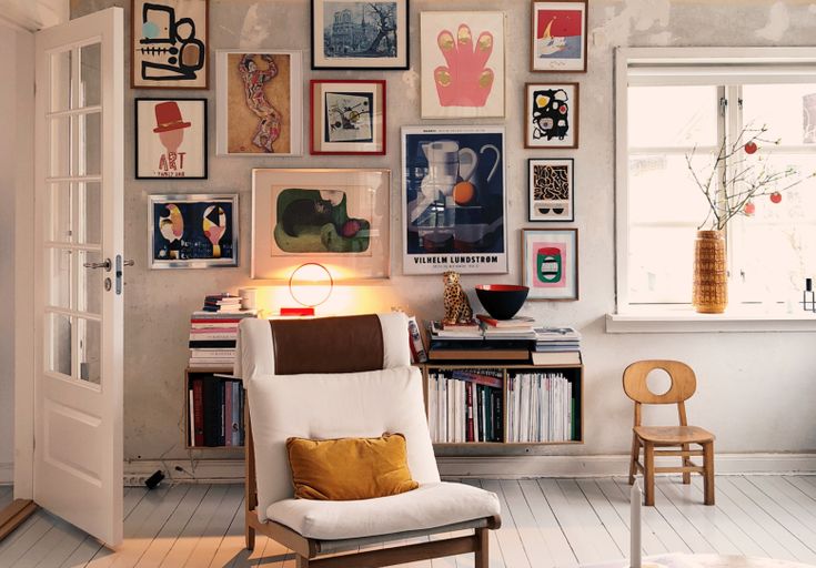 a living room filled with lots of pictures on the wall and a chair in front of it