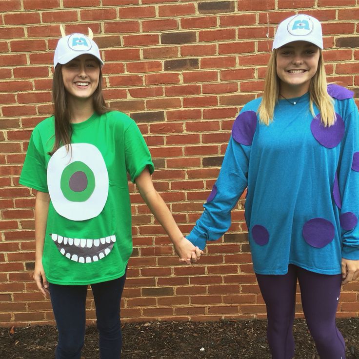 two girls in matching costumes hold hands and smile at the camera while standing next to a brick wall