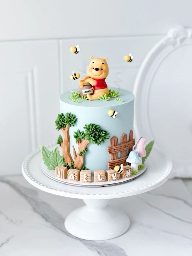 a winnie the pooh birthday cake is on a white pedestal with trees and bees around it