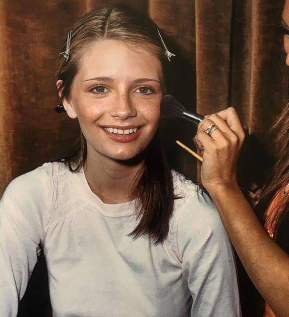 a woman is smiling as she brushes her face with a hair brush while another girl looks on