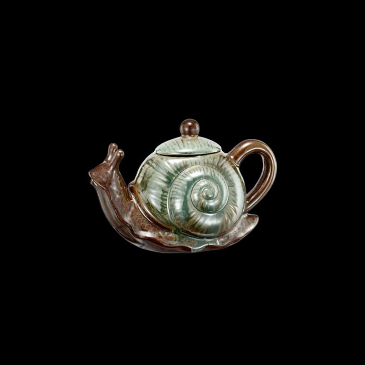 a ceramic teapot with a snail on it's side, against a black background