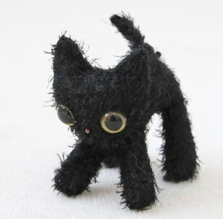 a small black cat with big eyes on a white surface