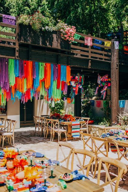 tables and chairs with colorful streamers hanging from the ceiling in front of a building