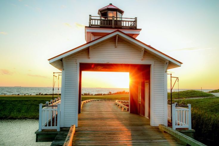 the sun is setting behind a small white building with a light house on it's roof