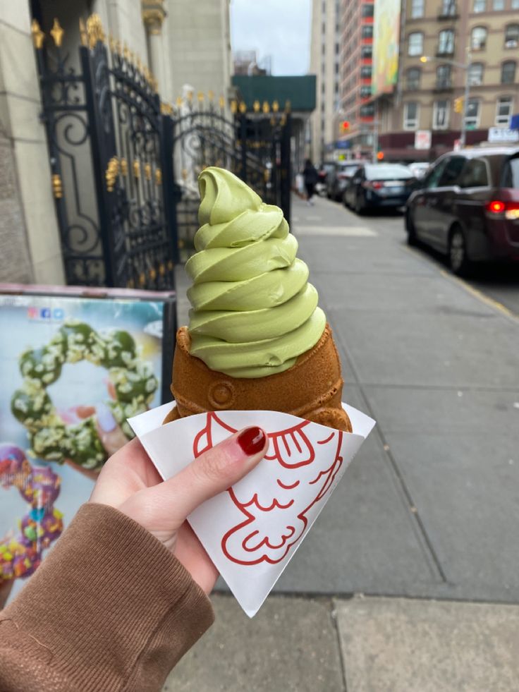 a person holding up an ice cream cone with green icing on it's top