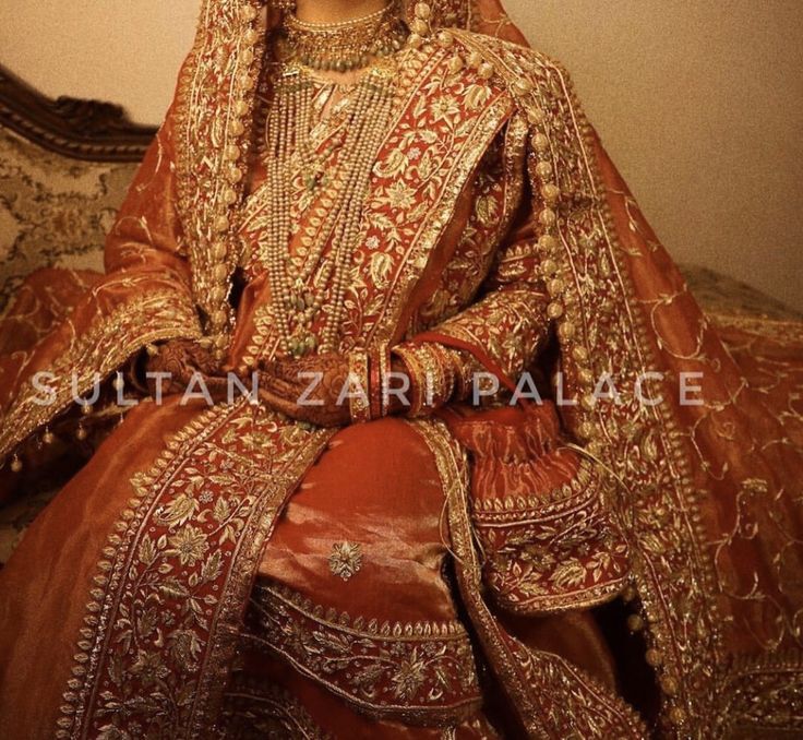 a woman in a red and gold bridal dress sitting on a couch with her hands behind her head