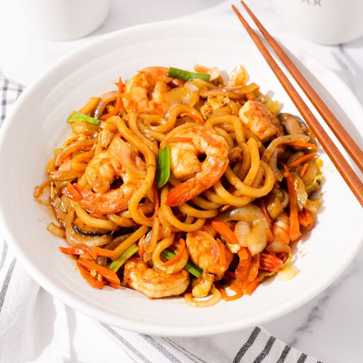 a white bowl filled with shrimp and noodles next to chopsticks on a table