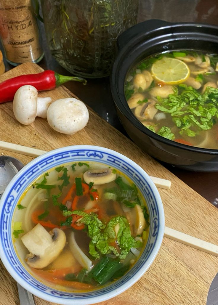 a bowl of soup with mushrooms, carrots and broccoli on the side