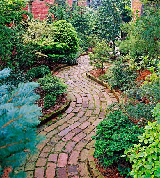 a brick path in the middle of a garden with trees and shrubs on either side