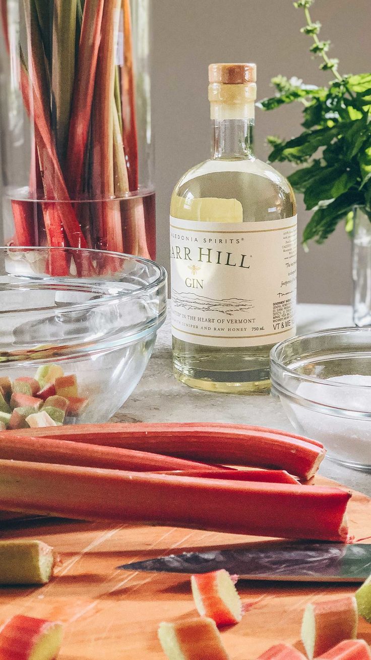 a bottle of gin sits on a table next to sliced rhubarb stalks