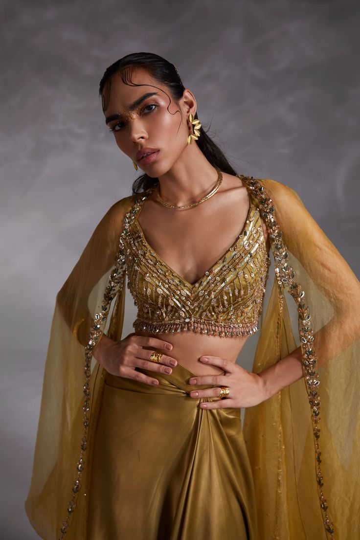 Editor's Note Featuring a ecru olive hand-embellished blouse with wide neckline, solid cape with hand embroidery detailing and asymmetrical drape skirt Color: Olive green Fabric: Heavy satin, organza Fit type: Blouse: fitted Neckline: V-neckline Components: Skirt, cape and blouse Occasion: Haldi mehndi, cocktail and wedding guest Care: Dry Clean Only About the Designer The crux and essence of the label, Divya Aggarwal, is to challenge and revamp the face of ordinary traditional wear while being Cape Organza, Blouse Yoke, Open Blouse, Padded Blouse, Wedding Blouse, Draped Skirt, Embellished Blouse, Desi Wedding, Yellow Blouse