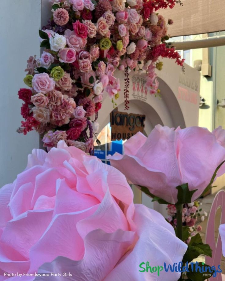 large pink flowers are in front of a store sign and wreath on the building's entrance