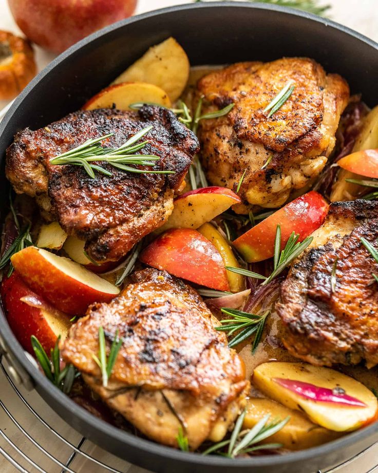 a pan filled with meat and vegetables on top of a wooden table next to an apple