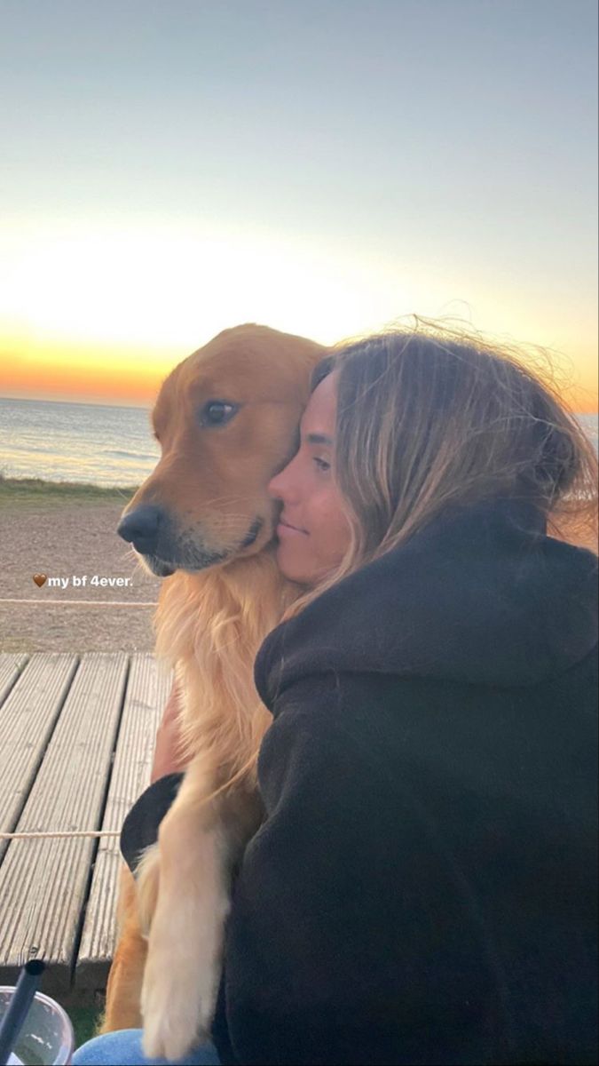 a woman is hugging her dog on the beach