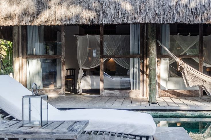 a bed sitting on top of a wooden floor next to a pool in front of a hut