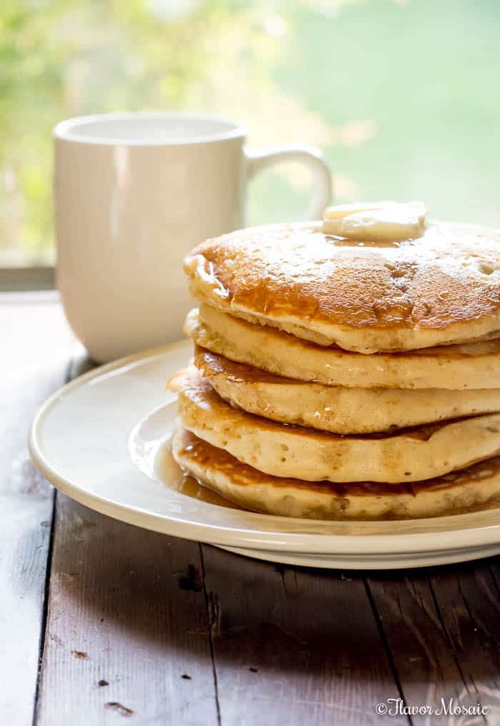 a stack of pancakes sitting on top of a white plate next to a coffee cup