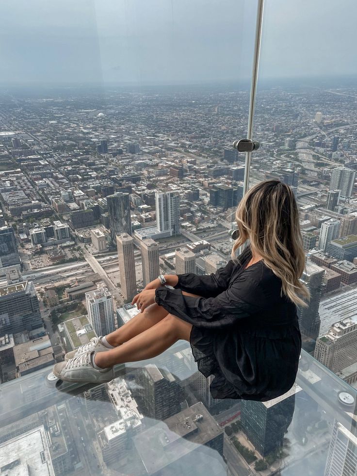 a woman sitting on top of a tall building looking down at the city from above