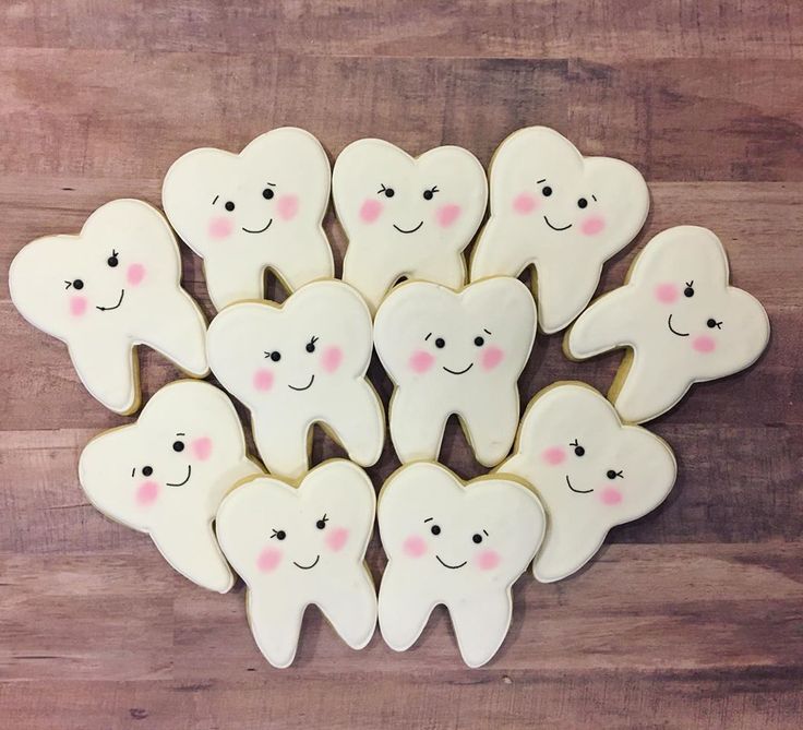 decorated cookies in the shape of teeth are arranged on a wooden table with pink dots