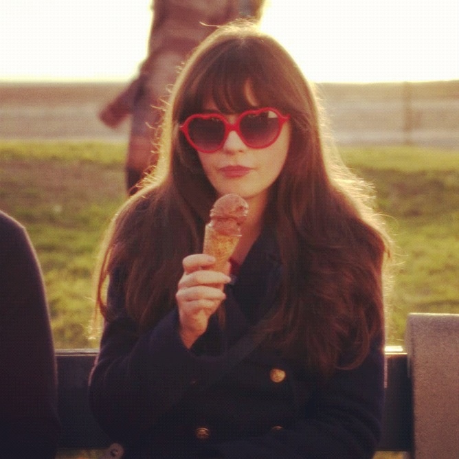 a woman in sunglasses eating an ice cream cone on a park bench with people behind her