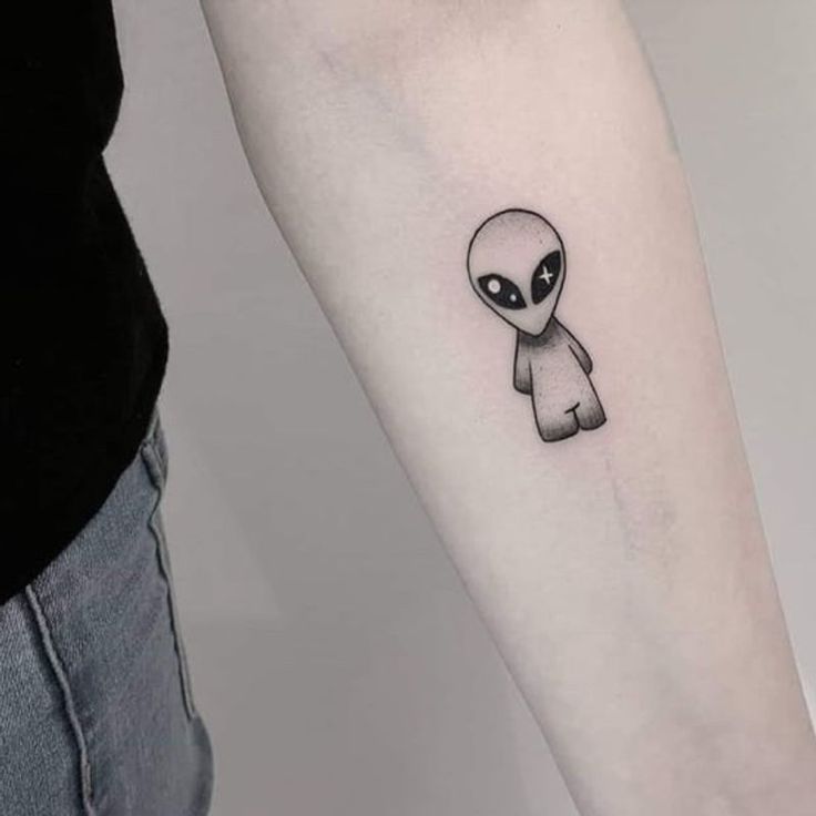 an alien tattoo on the left inner forearm and arm, with a small black dot in the center