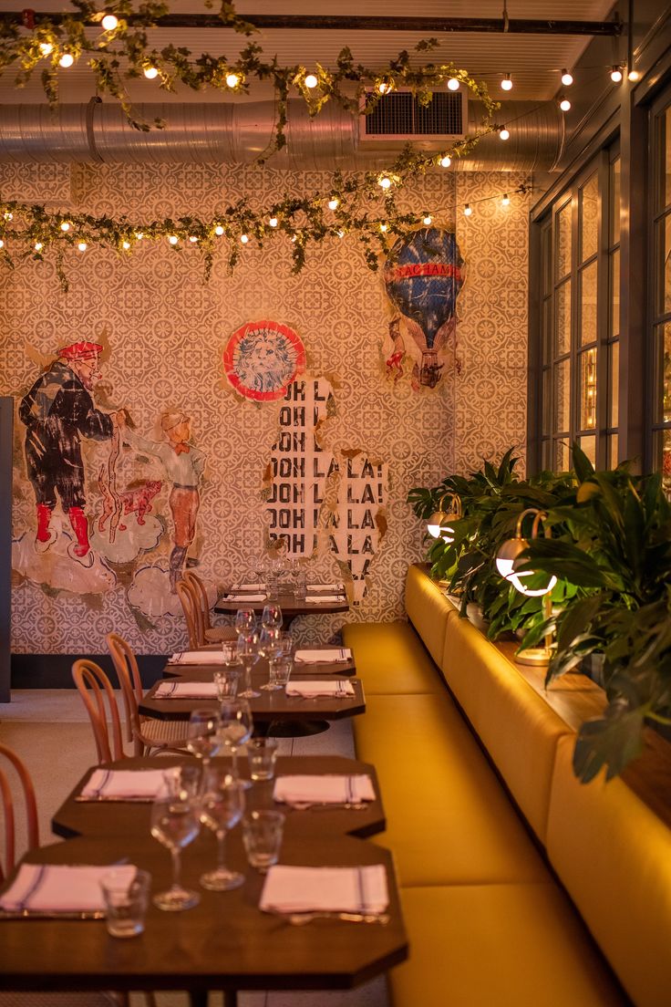 an empty restaurant with tables and chairs covered in plants, lights and artwork on the wall