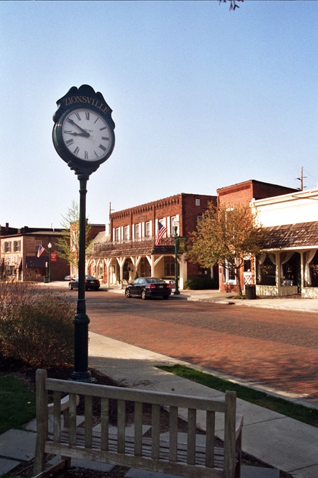 a clock on a pole in the middle of an empty street with buildings behind it