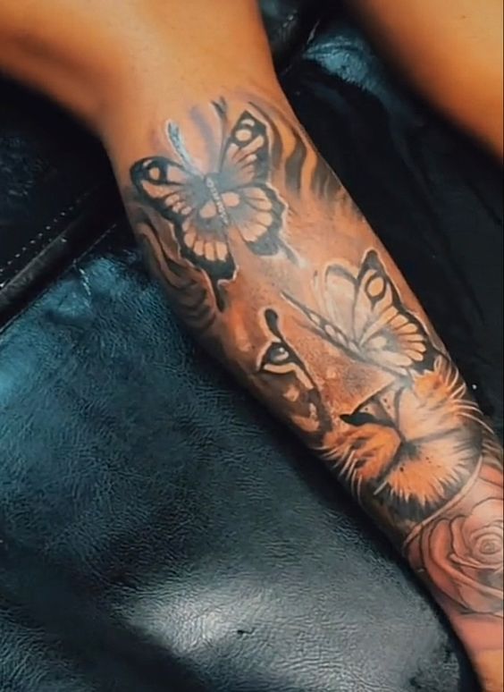 a person with a tiger and butterfly tattoo on their arm, sitting down next to a black leather couch