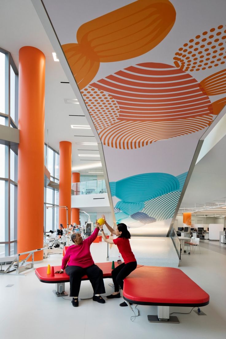 two women are sitting on benches in an office building and one is holding up a yellow object