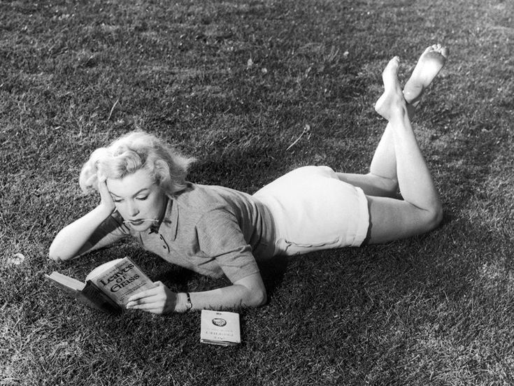 a woman laying on the grass reading a book