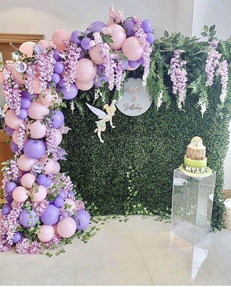 the balloon arch is decorated with purple and pink balloons, greenery, and a fairy tale cake