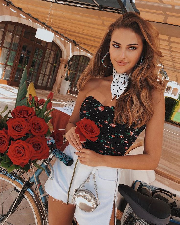 a beautiful young woman standing next to a bike with roses in her basket on it