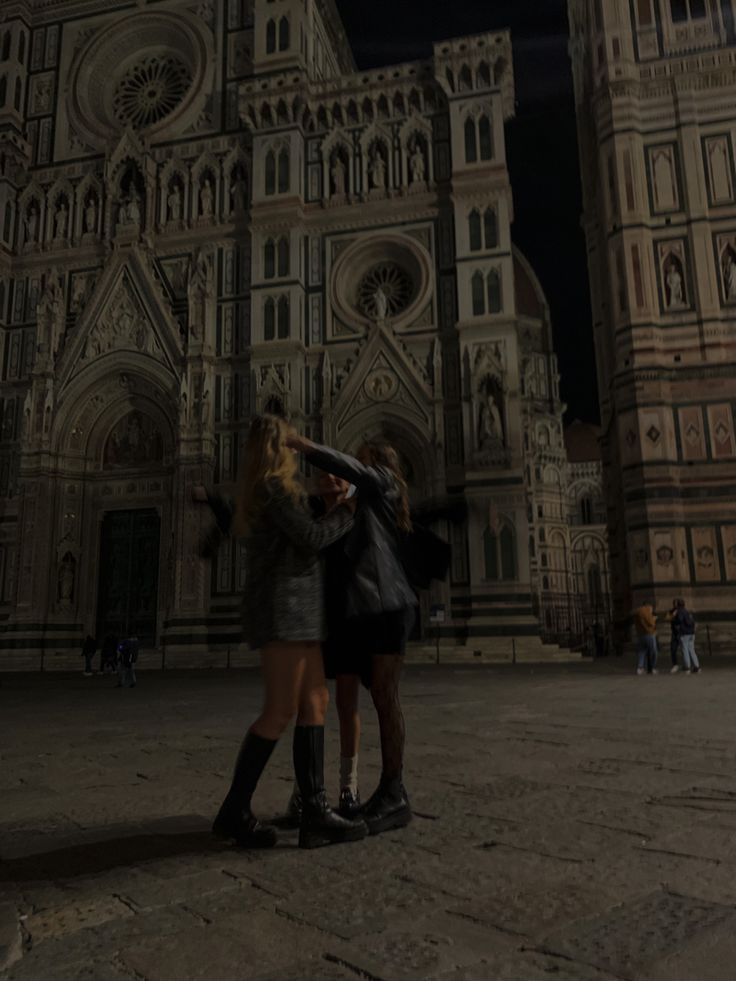 two women standing in front of a cathedral at night with their arms around each other