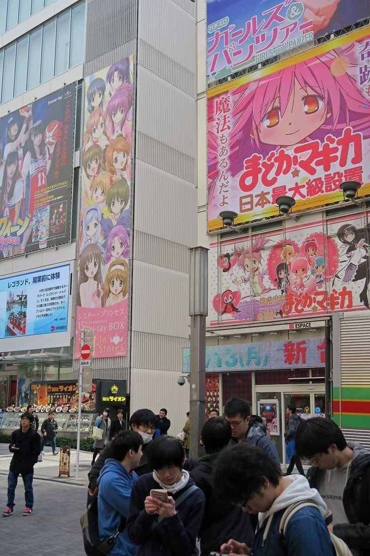 many people are standing on the sidewalk in front of tall buildings with advertisements above them