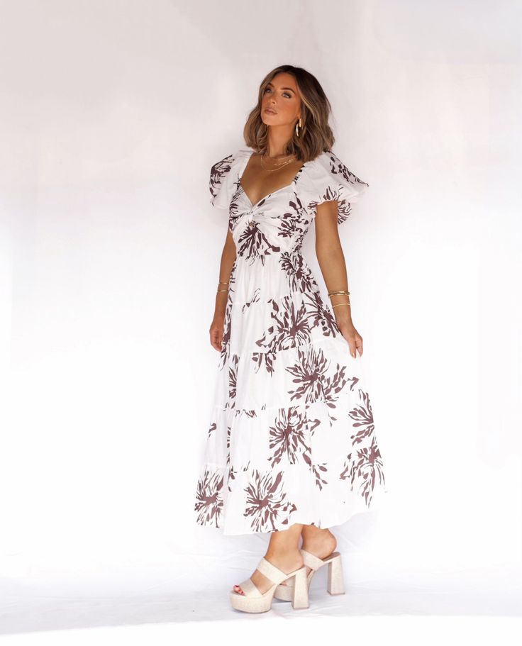 a woman in a white and brown floral print dress is standing with her hands on her hips