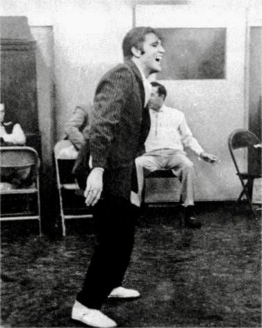 an old black and white photo of two men singing in a room with other people