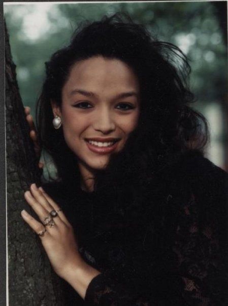 a woman is smiling and leaning against a tree