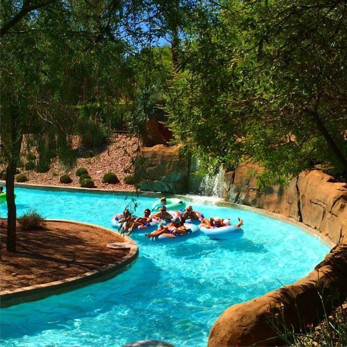 several people are on rafts in the water at an outdoor swimming pool that is surrounded by trees and rocks