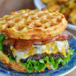 a waffle sandwich on a blue plate with other food items in the back ground