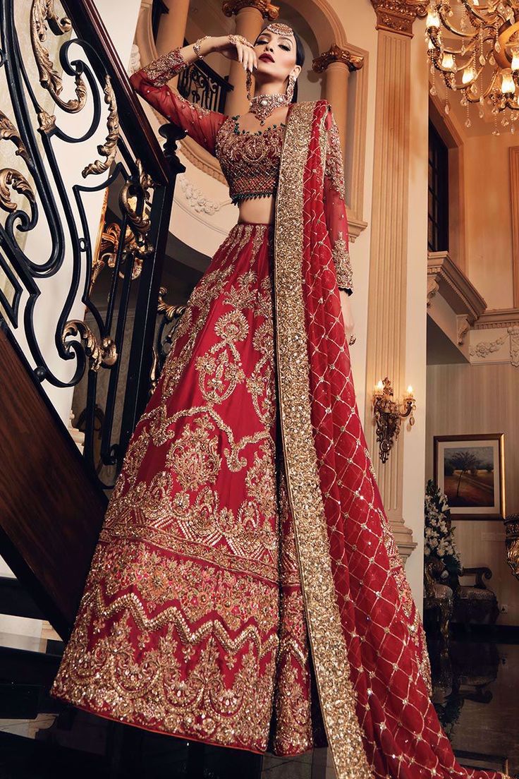 a woman in a red and gold bridal gown standing on stairs with her hands behind her head