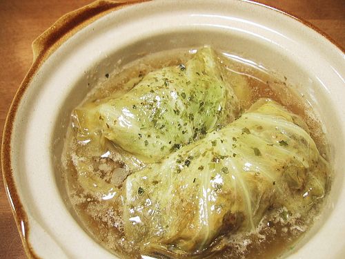 two stuffed cabbages are in a bowl with broth and sauce on the side