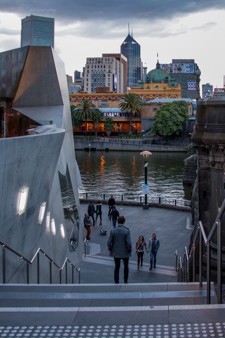 people are walking up and down the stairs in front of a river with buildings on both sides