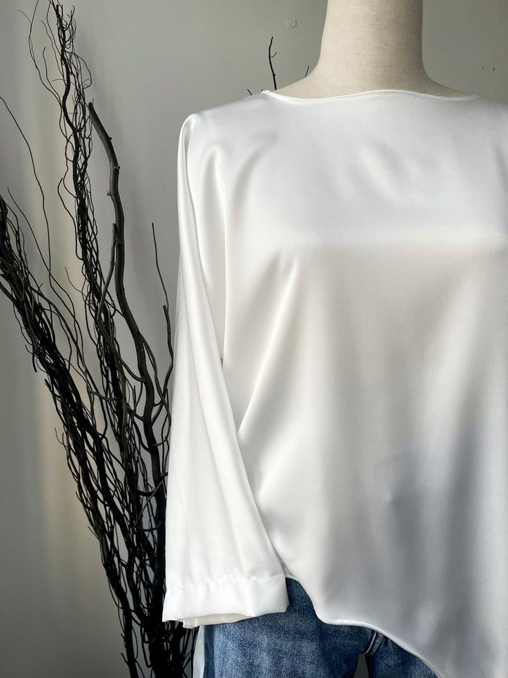 Introducing our stunning White Long Blouse, crafted with utmost elegance and made from luxuriously soft satin material. This versatile wardrobe essential is designed to effortlessly elevate your style and provide unmatched comfort throughout the day. The front of this exquisite blouse features a gracefully curved cut that starts at the waist and cascades down to the bottom, adding a touch of sophistication to your ensemble. The unique curve emphasizes your natural waistline, creating a flattering silhouette that complements all body types. Indulge in the unparalleled softness of the satin material that glides against your skin, offering a gentle and sensual embrace throughout the day. The silky texture not only feels incredibly soft but also adds a touch of glamour to your outfit, making t Sleek Solid Silk Blouse, Chic Long Sleeve Plain Blouse, Sleek Silk Top With Satin Finish, Classic Satin Top With Satin Finish, Elegant White Plain Blouse, Elegant Plain White Blouse, Long Sleeve Satin Finish Top For Formal Occasions, Formal Long Sleeve Top With Satin Finish, Long Sleeve Tops With Satin Finish For Formal Occasions