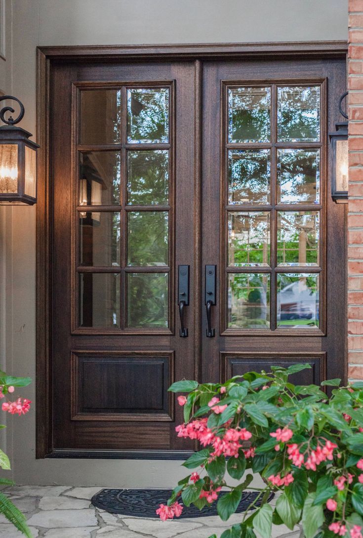 the front door to a house with two lights on it and pink flowers growing outside