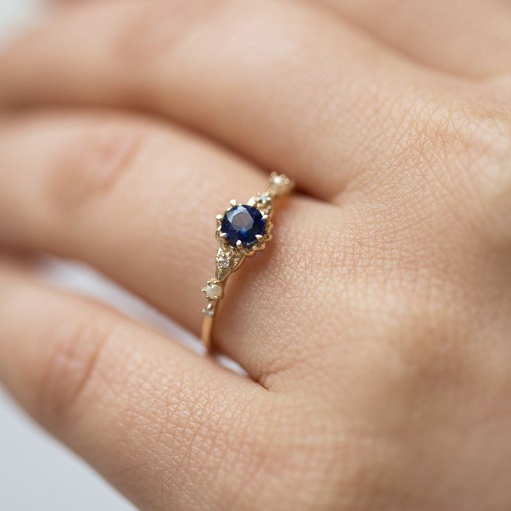 a woman's hand with a gold and blue ring on her finger, showing the center stone