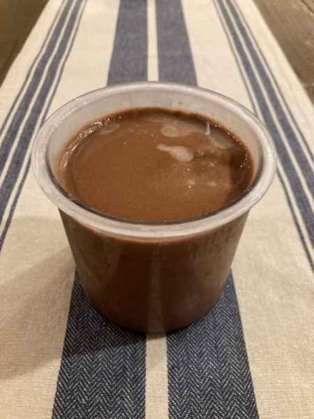 a plastic cup filled with chocolate sitting on top of a striped tablecloth covered table